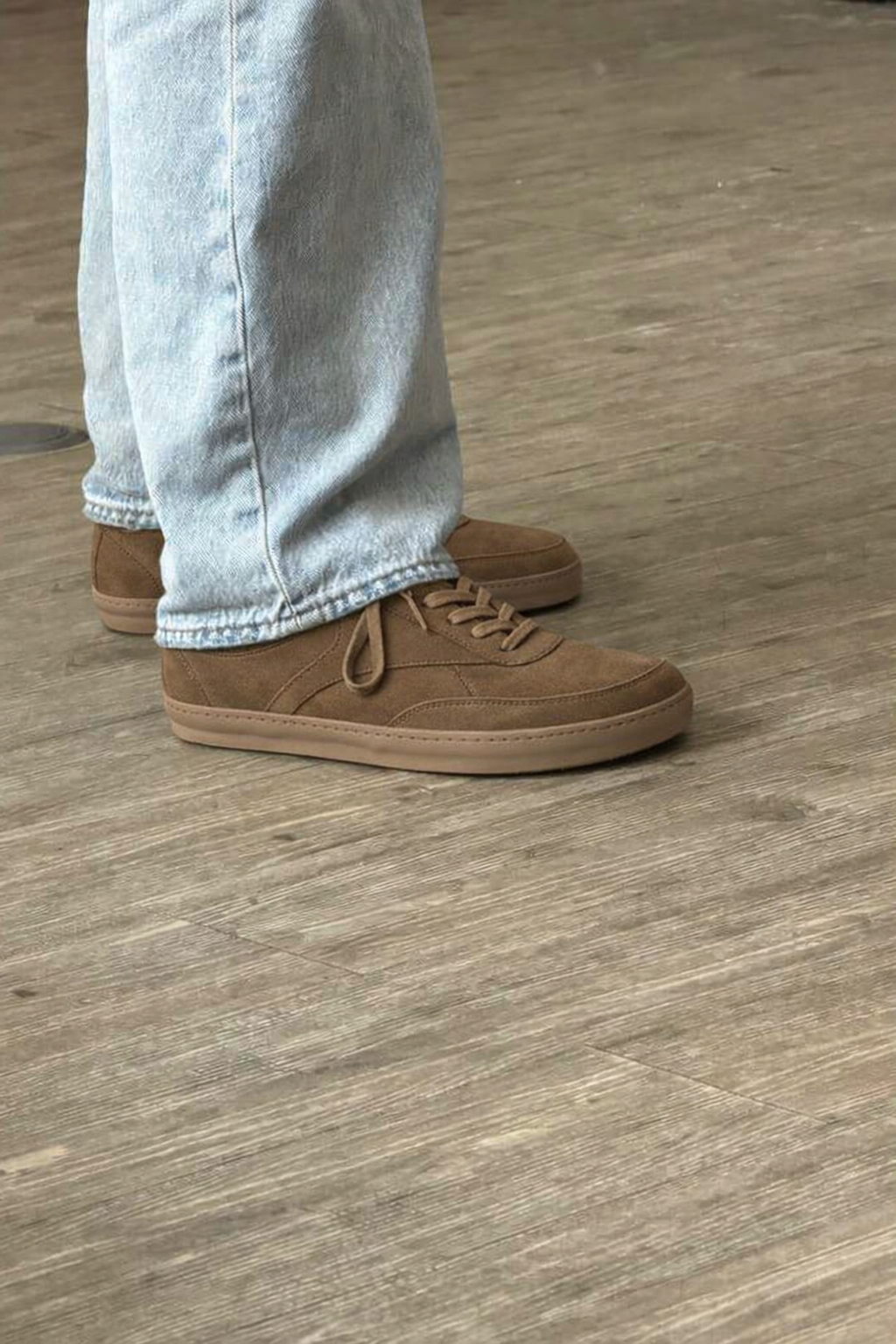 Brown suede shoes worn with light blue jeans on a wooden floor.